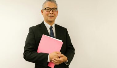 Confident businessman in black suit holding pink folder, smiling at the camera indoors.